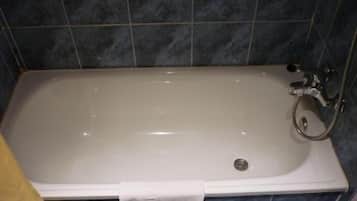 Un baño con una bañera blanca, azulejos azul oscuro y una toalla blanca colgada a un lado.