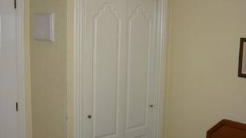 Une pièce avec une armoire blanche, un lit recouvert d’une couverture verte et une tête de lit en bois.