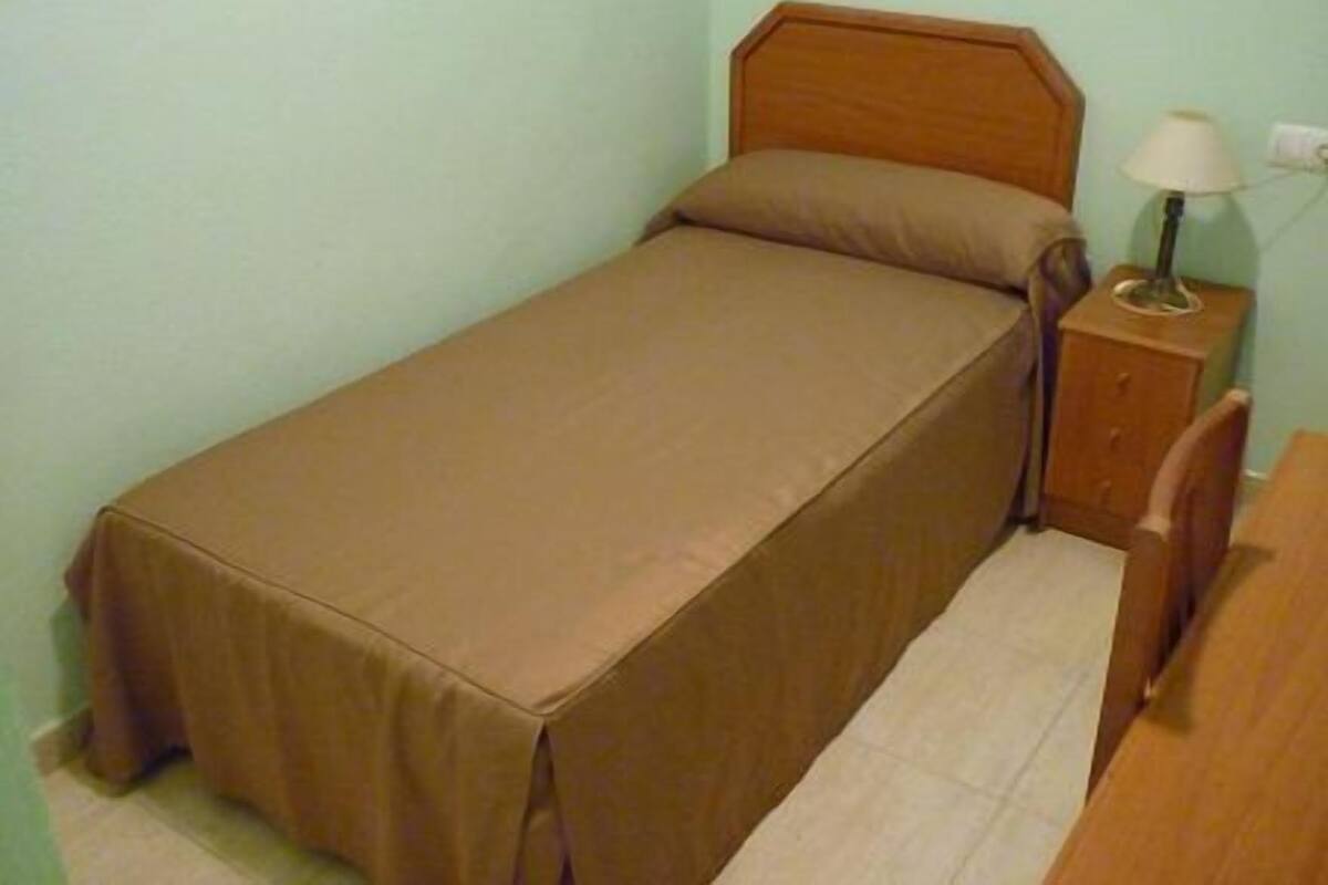 Ein Einzelbett mit Holz-Kopfteil, ein Nachttisch mit Lampe und ein Sessel.