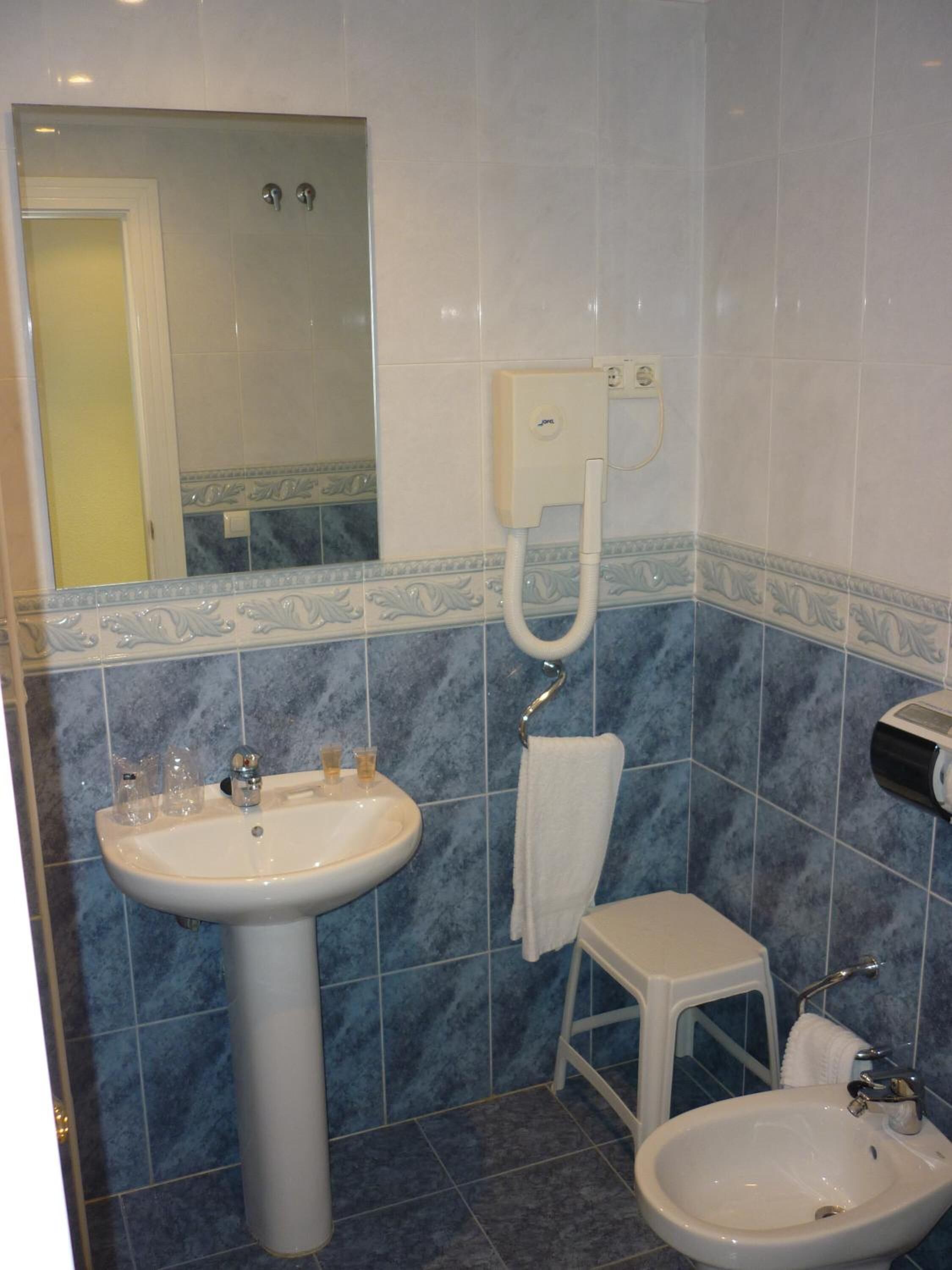 Un baño con lavamanos pedestal, lavamanos en esquina, inodoro y ducha.