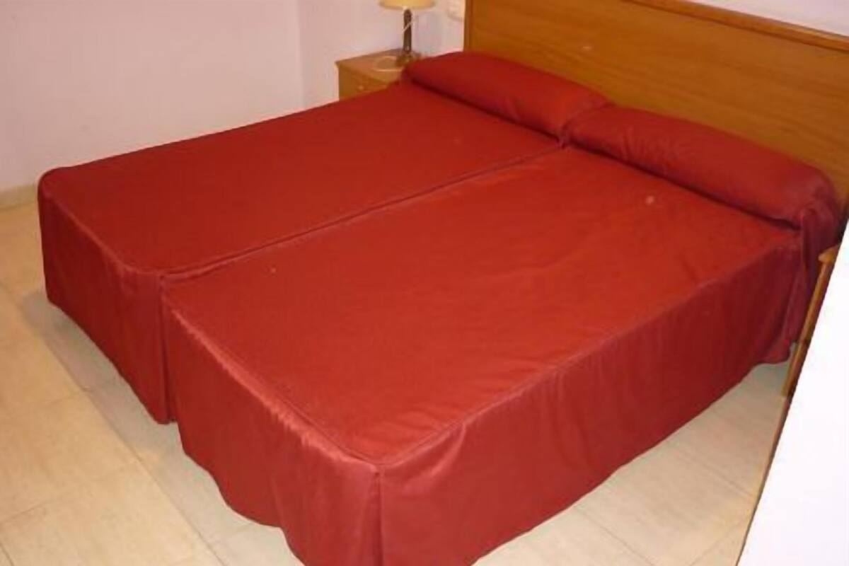 Ein Einzelbett mit roter Bettdecke in einem Zimmer mit Fliesenboden.