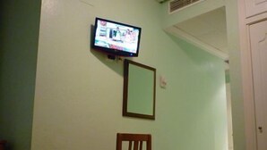 A room with a television mounted on the wall, a wooden chair, and a small shelf. - Hotel Tuto (Torrevieja)