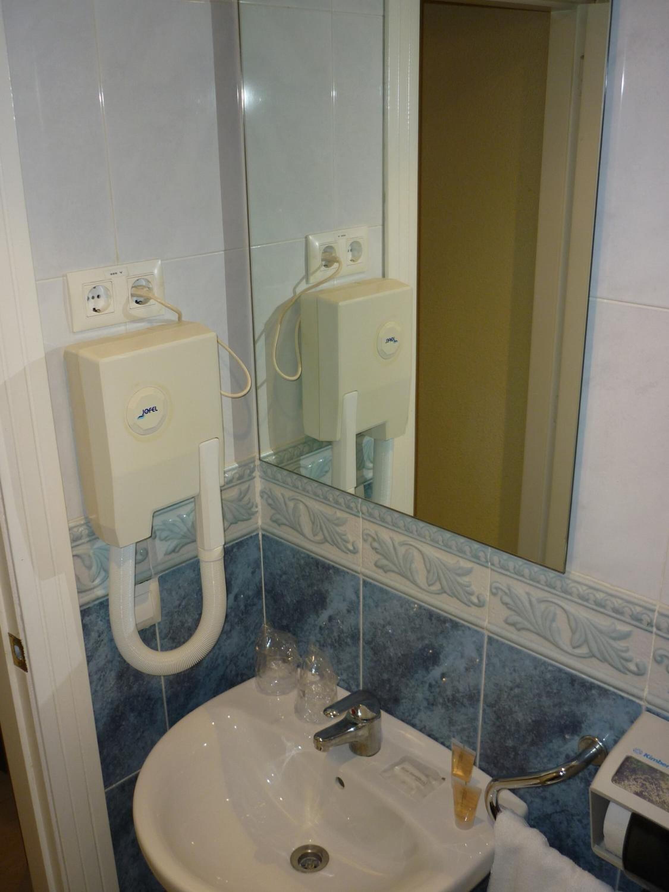 A bathroom with a sink, mirror, and two wall-mounted soap dispensers.