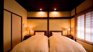 A hotel room with two beds, wooden headboards, bedside lamps, and a shoji screen. - Kazueya (Kanazawa)