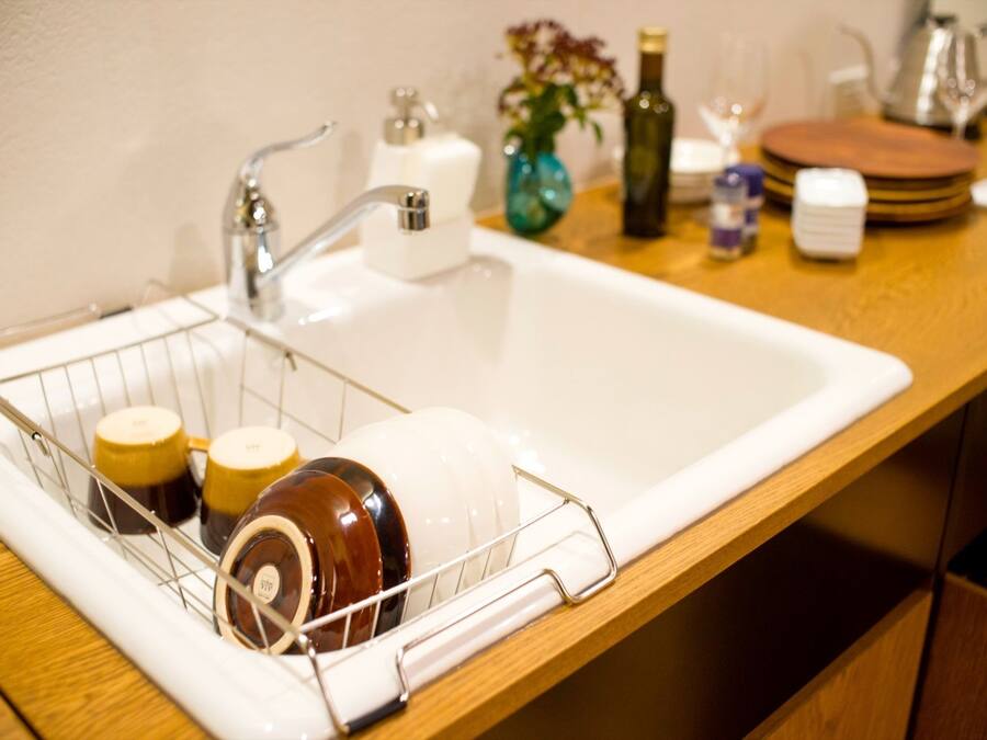 A kitchen sink with a dish rack holding mugs and a bottle.
