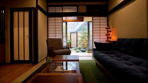 A traditional Japanese interior with tatami flooring, a low table, a sofa, and sliding doors leading to a garden. - Kazueya (Kanazawa)