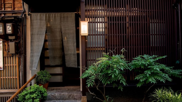 A traditional Japanese entrance with a wooden gate, a stone staircase, and potted plants. - Kazueya (Kanazawa)