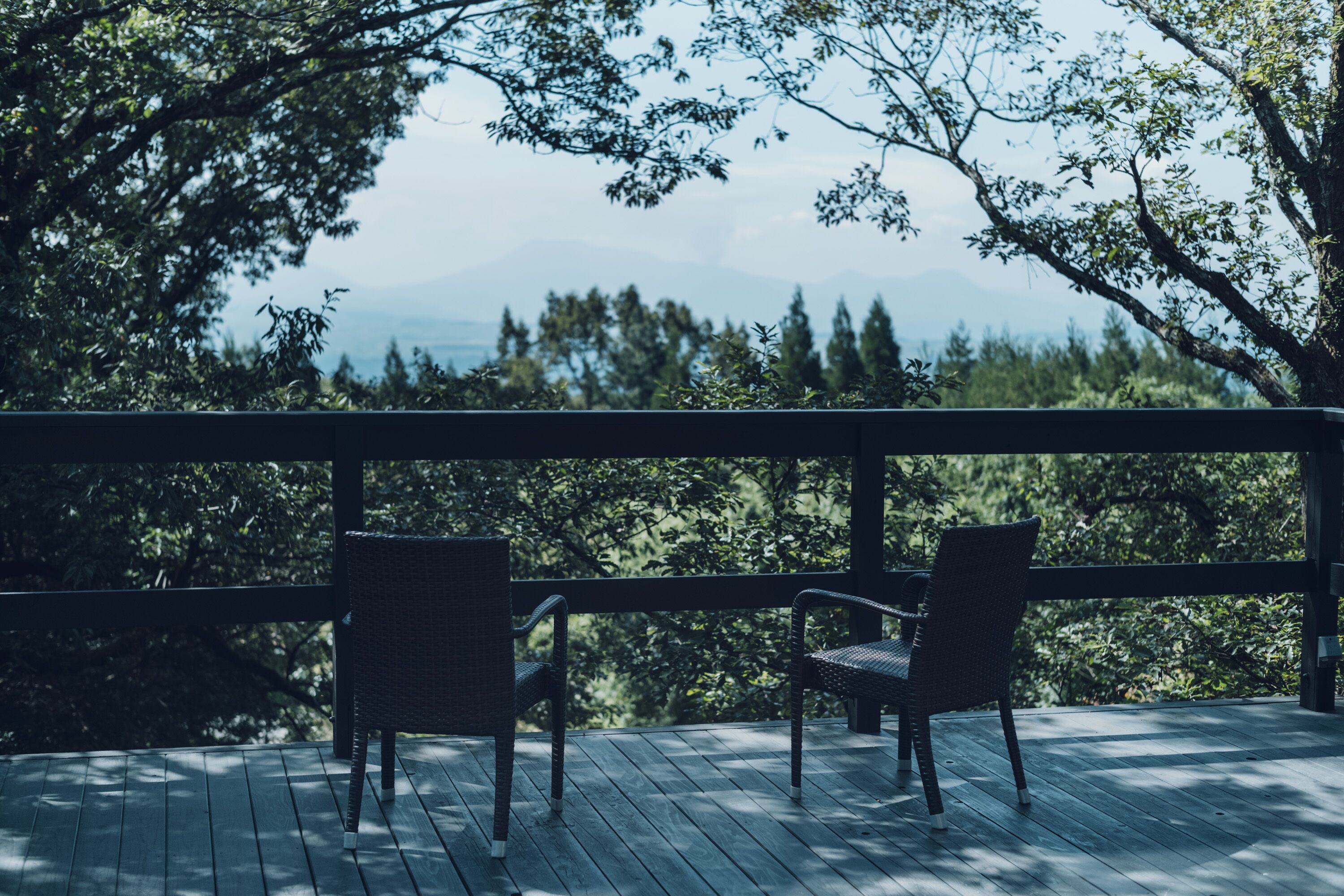 A wooden deck with two wicker chairs facing a forested landscape.