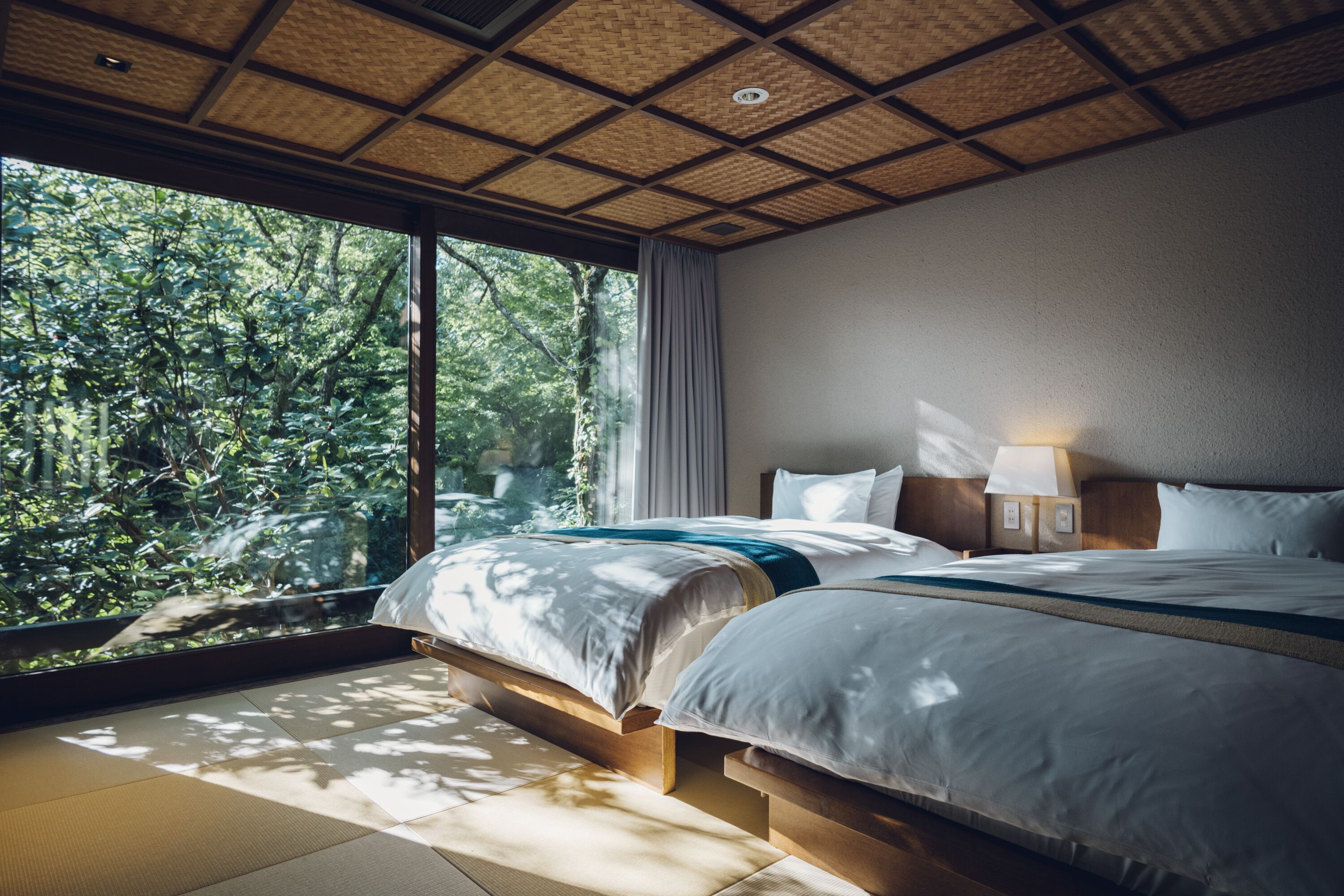 A bedroom with a large window, wooden flooring, and a bed with a blue accent.