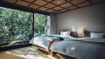 A bedroom with a large window, wooden flooring, and a bed with a blue accent.