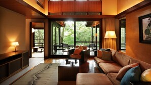 A modern interior with a sofa, coffee table, and lamps. There is a view of greenery outside through large windows. - Hoshino Resorts KAI Aso (Kokonoe)