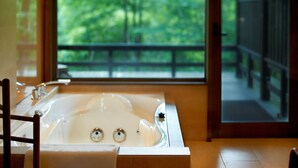A bathroom with a large bathtub, a wooden chair, and a view of a balcony with a railing. - Hoshino Resorts KAI Aso (Kokonoe)