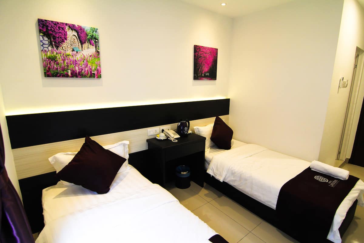 A hotel room with two beds, a nightstand with a phone and a kettle, and two paintings on the wall.