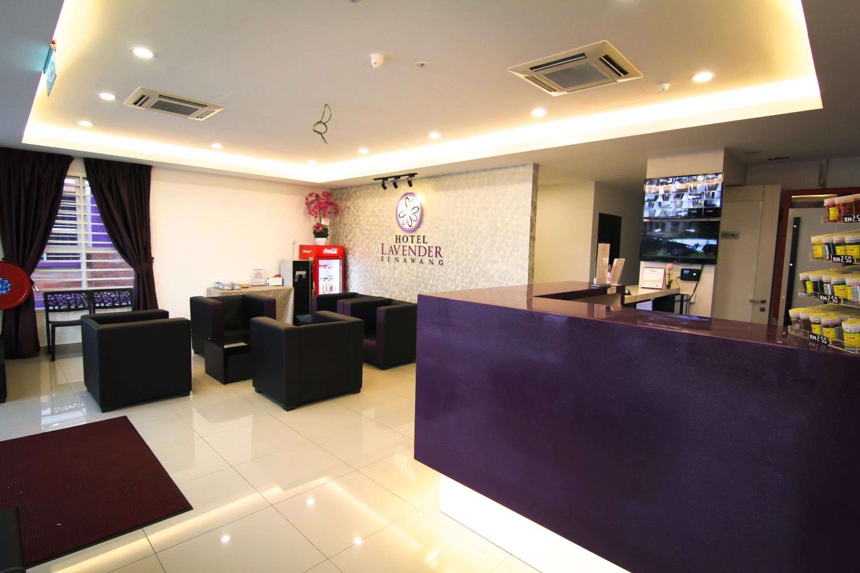 A hotel reception area with a purple counter, seating area, and a wall-mounted TV.