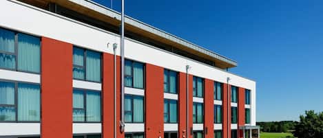 Un edificio moderno con techo plano, ventanas grandes y fachada roja y blanca.