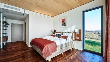 Un dormitorio moderno con una cama grande, suelo de madera, vistas al exterior y una escalera que lleva a otra habitación.
