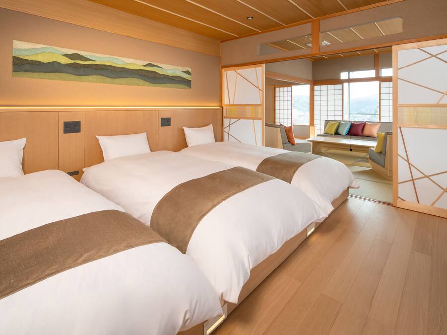 A hotel room with two large beds, a wooden ceiling, a view of the city, and a traditional Japanese sliding door.
