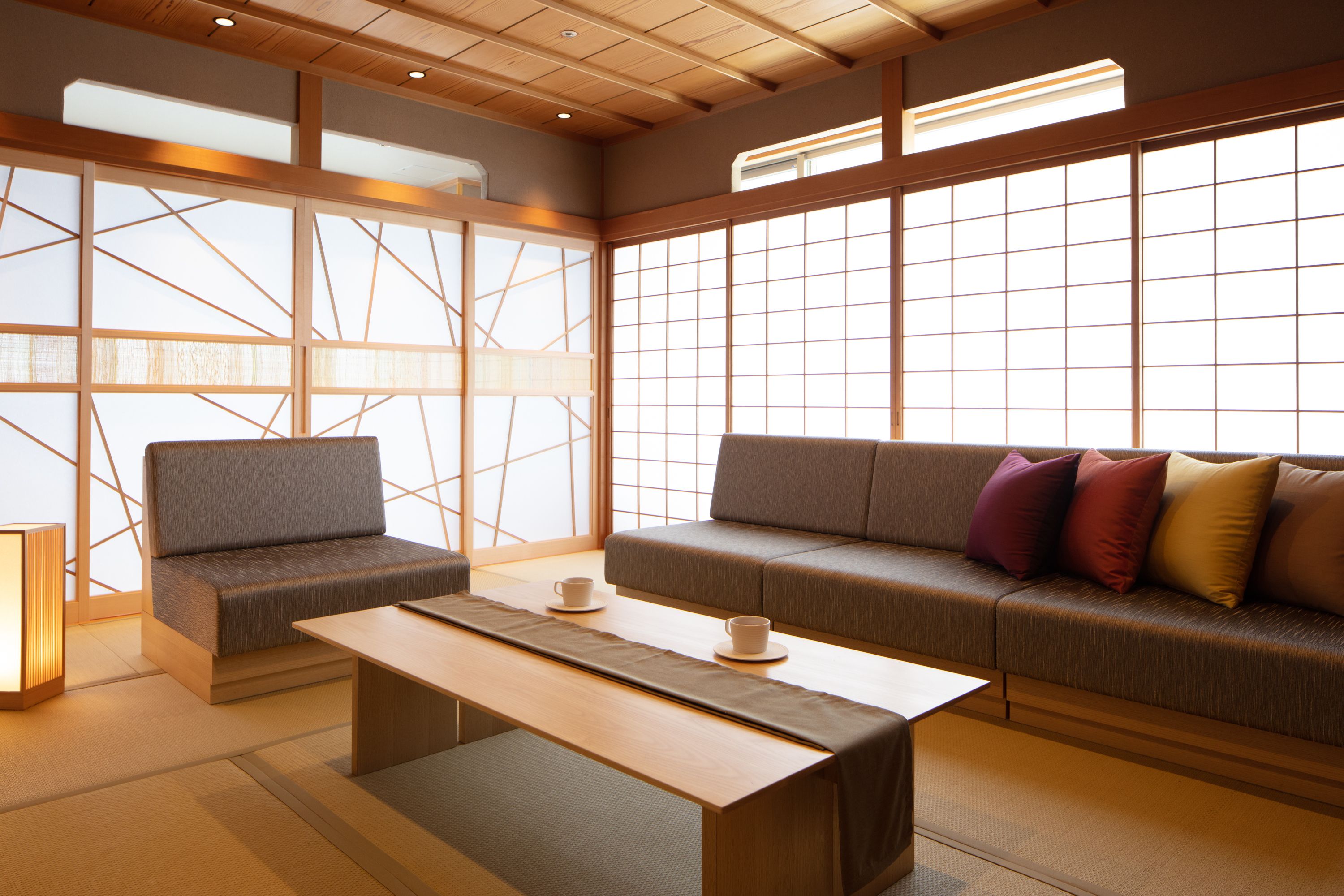 A traditional Japanese-style room with tatami flooring, a low table, a sofa with cushions, and sliding shoji doors.