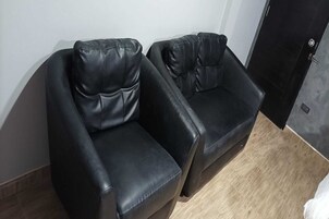 Dos sillones de cuero negro en un rincón de una habitación con piso de madera y pared blanca.