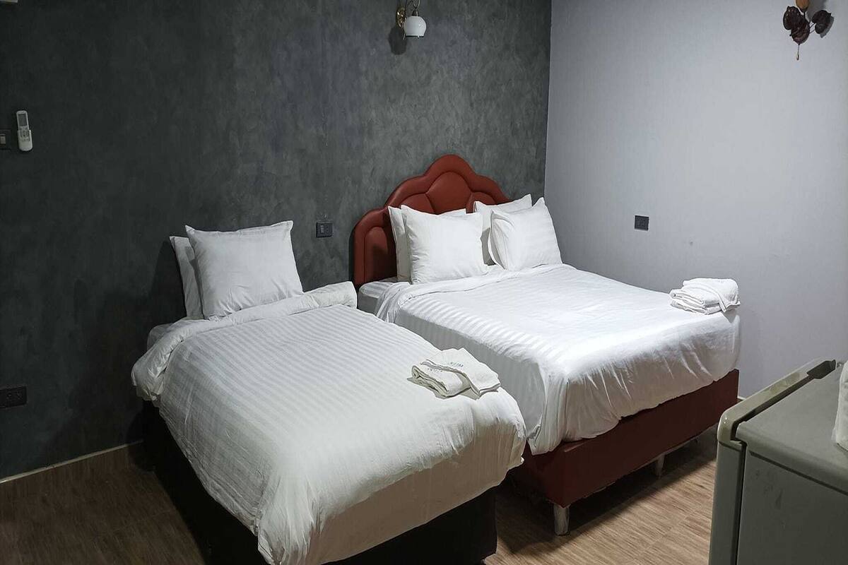 Habitación de hotel con dos camas, cada una con ropa blanca de cama y almohadas, cabeceros rojos y una mesita de noche con una lámpara.
