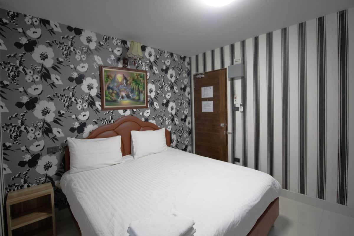 Un dormitorio con cama, cabecera de madera, mesita de noche, un cuadro en la pared y una puerta con estampado a rayas.