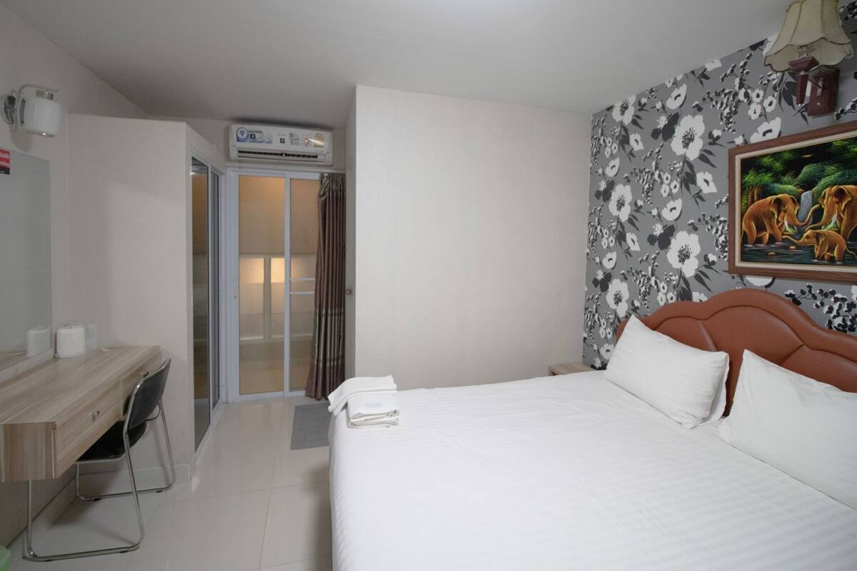 Una habitación de hotel con una cama, un escritorio con una silla, una zona de ducha y un adorno floral en la pared.
