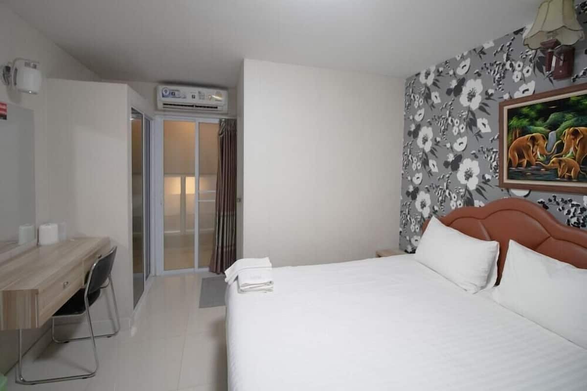 Habitación de hotel con cama, escritorio, silla, ducha y pared decorada con un estampado floral y un cuadro.