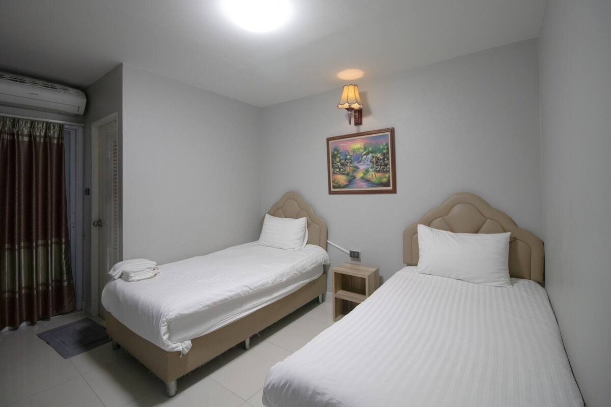 Habitación de hotel con dos camas, un cuadro en la pared, una mesita de noche y una ventana con cortinas.
