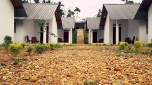 A building with a gravel courtyard, multiple rooms with doors, and a central pathway leading to a covered area. - Sinharaja Forest Sanctuary Hotel (Deniyaya)