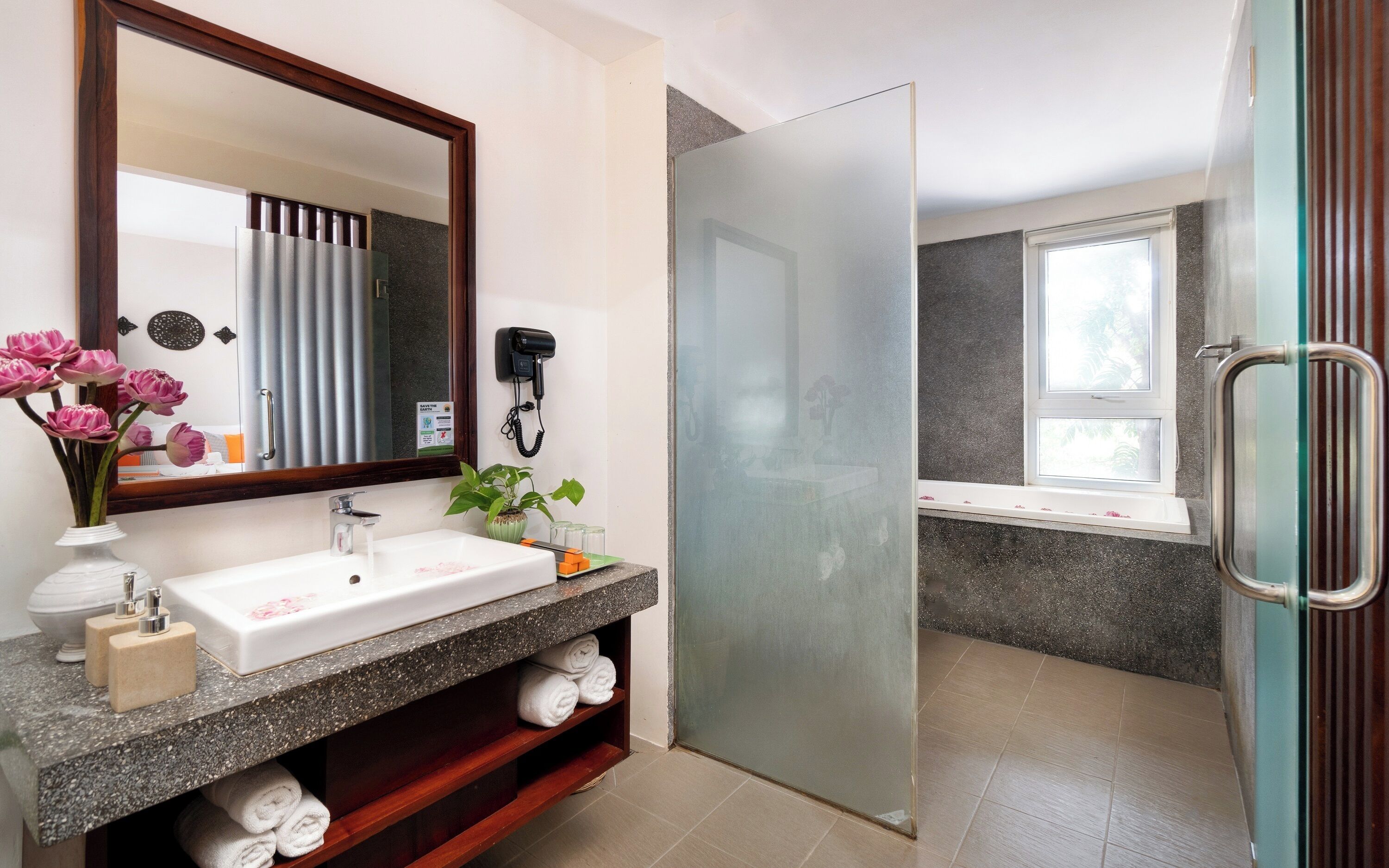 A bathroom with a white sink, a mirror, a telephone, a potted plant, and a shower area.