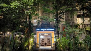 La entrada a Indra Angkor Residence, con un exuberante jardín y escalones que conducen a la entrada, rodeada de follaje denso y una fachada bien iluminada.