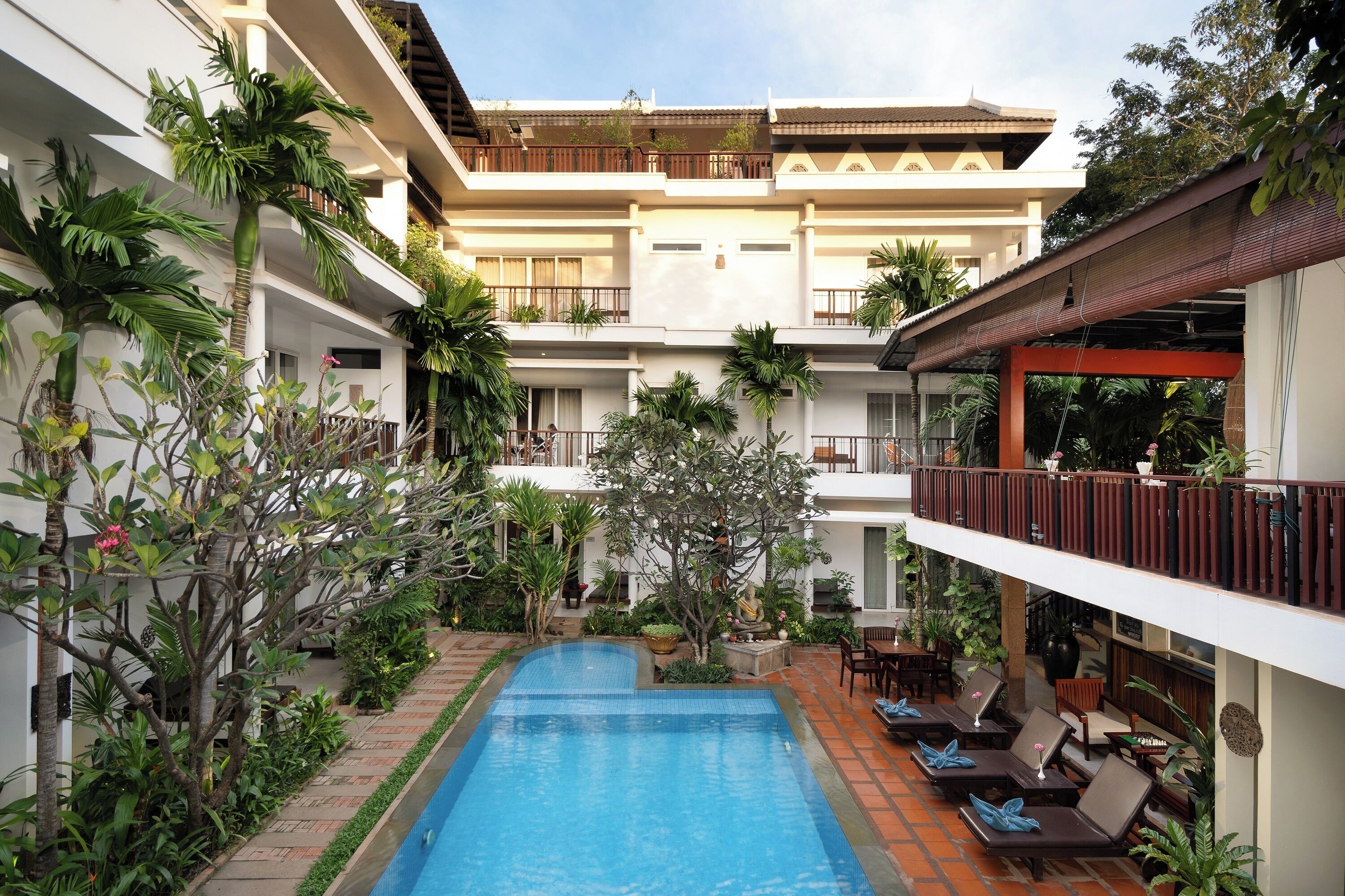 A multi-story hotel with a central swimming pool, outdoor seating, and lush greenery.