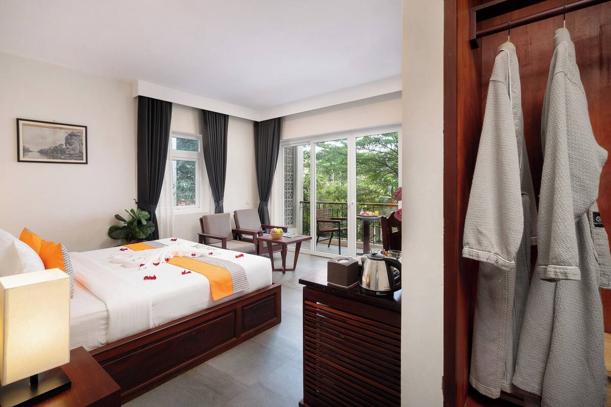 Ein Hotelzimmer mit Bett, Schreibtisch, Stuhl, Tisch und einem Balkon mit Blick auf Grünflächen.