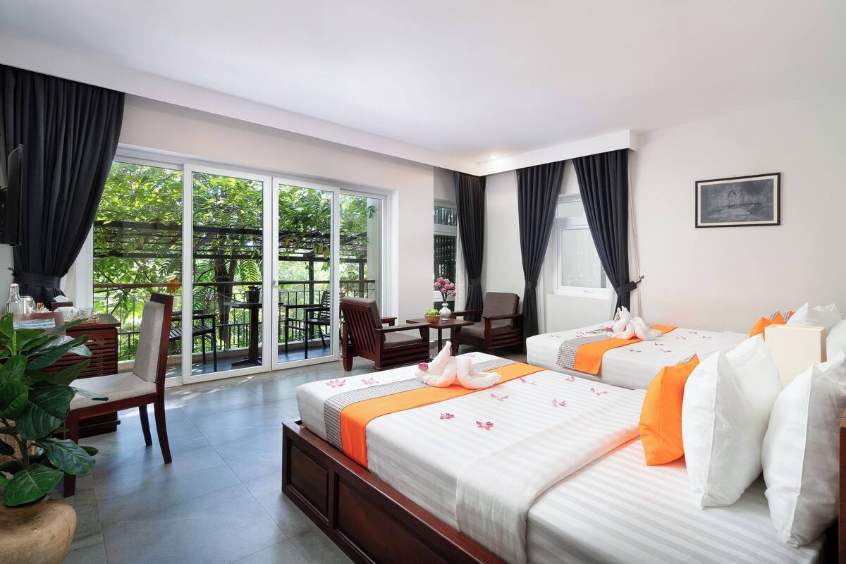 Ein Hotelzimmer mit zwei Betten, einem Balkon mit Tisch und Stühlen und Blick auf Grünflächen.
