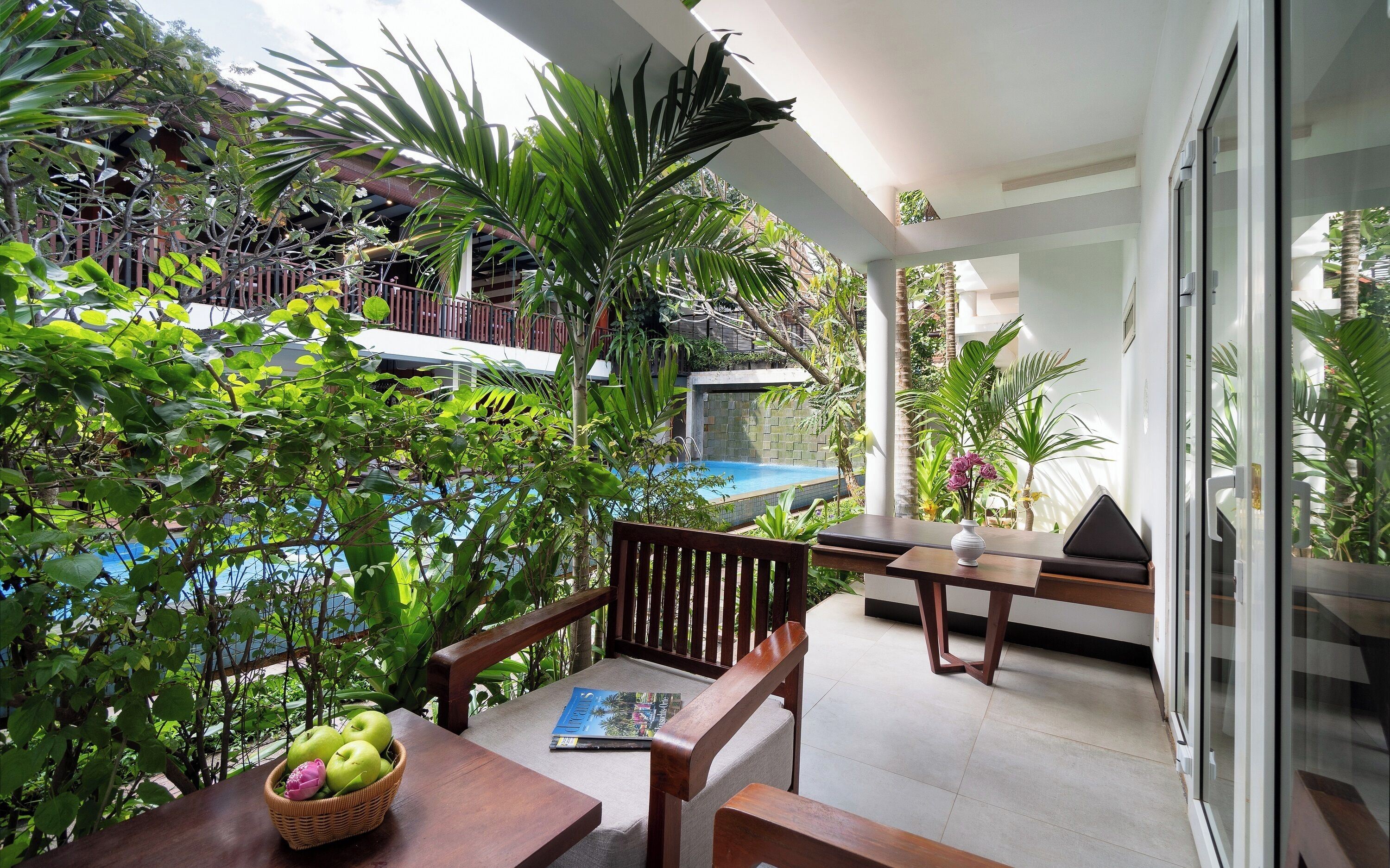 A balcony with a pool, surrounded by lush greenery and wooden furniture.