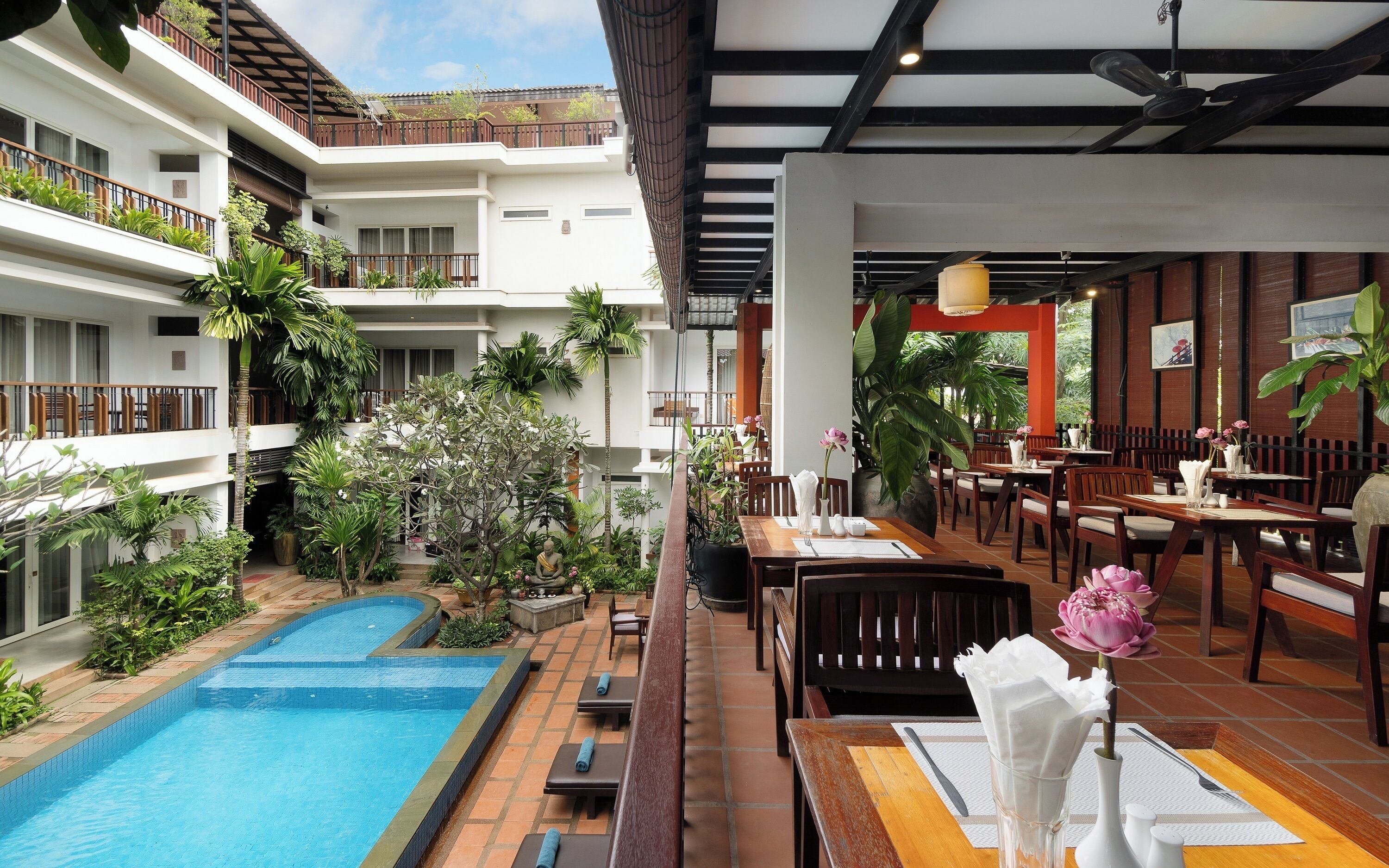 A hotel with a swimming pool, outdoor dining area, and multiple floors with balconies.