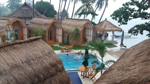 A tropical resort with thatched-roof cottages, a swimming pool, and palm trees. - The Place Beach Bungalows (Sekotong Barat)