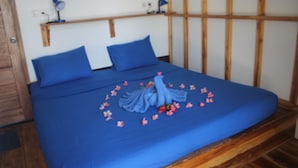 A bed with blue bedding and pillows, a wooden headboard, and a wall-mounted shelf with lamps. - The Place Beach Bungalows (Sekotong Barat)