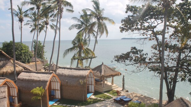 A beachfront property with thatched-roof cottages, a swimming pool, and palm trees. - The Place Beach Bungalows (Sekotong Barat)