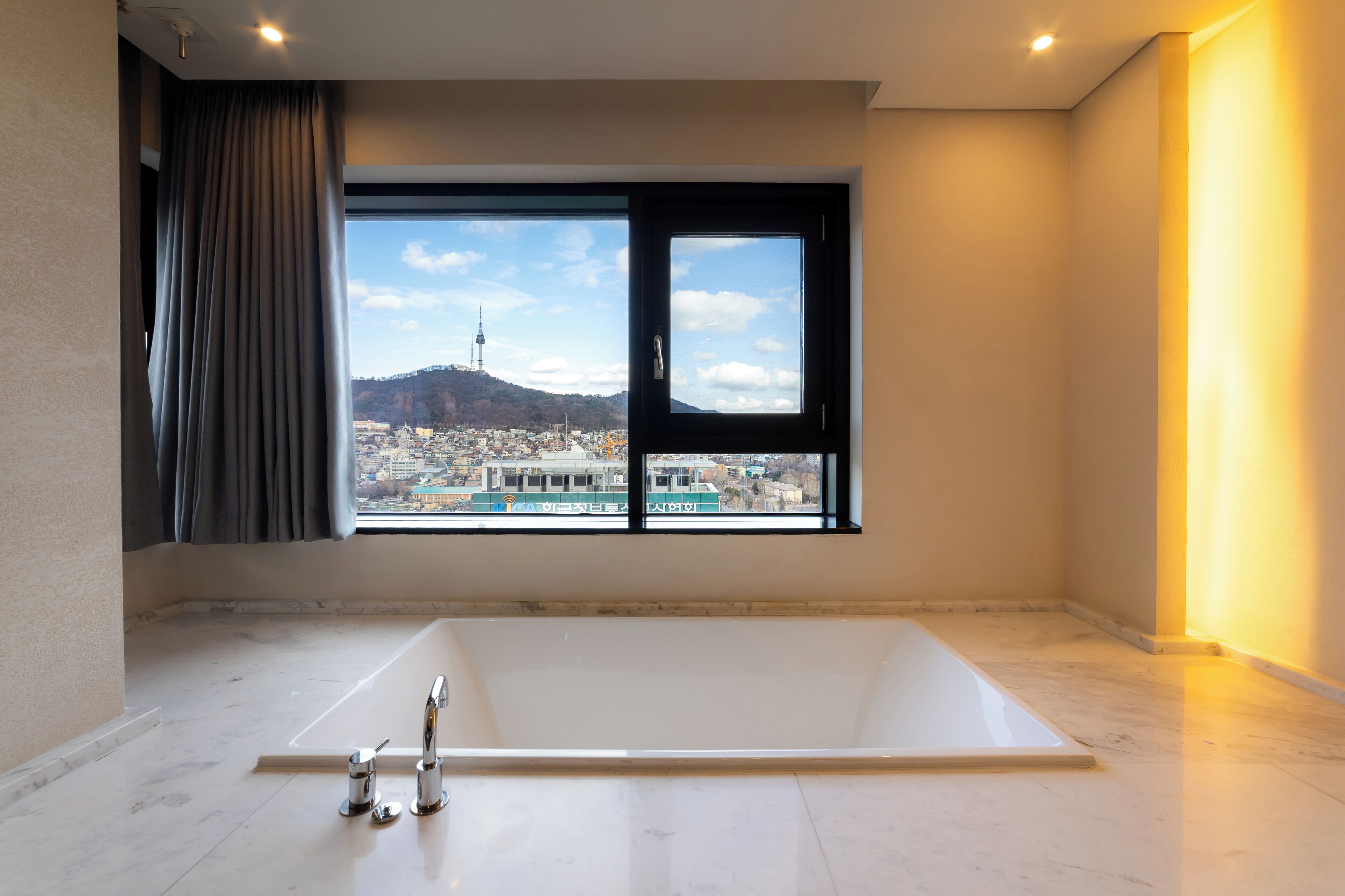 A modern bathroom with a large bathtub, a window with a city view, and a curtain.
