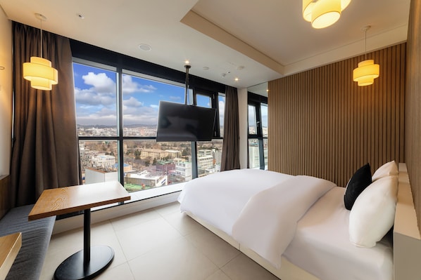 A modern hotel room with a large bed, a desk, and a TV.