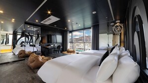 Una habitación de hotel moderna con una cama grande, pufs, un escritorio y vistas a la ciudad.