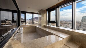 Un baño moderno con una bañera grande, múltiples grifos y vistas a la ciudad a través de amplias ventanas.
