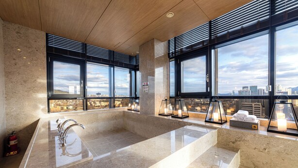 Un baño moderno con un lavabo de mármol grande, varias ventanas y vistas a la ciudad.