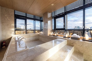 A modern bathroom with a large marble sink, multiple windows, and a city view.