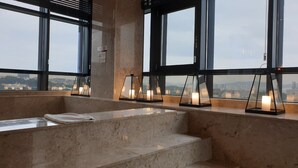 Un baño moderno con encimera de mármol, una bañera y tres velas encendidas sobre un repisa.