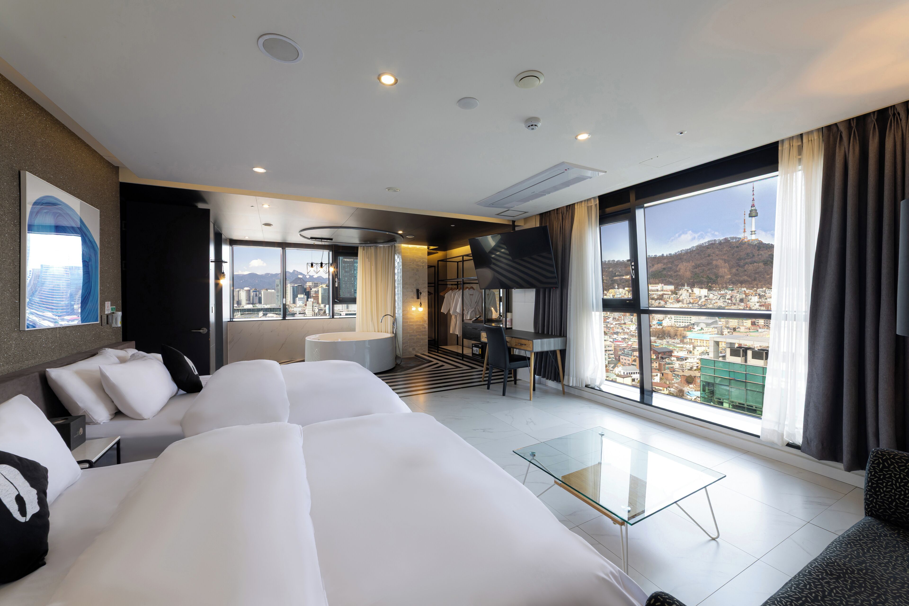 Una habitación de hotel moderna con una cama grande, un escritorio y vistas a un paisaje urbano.