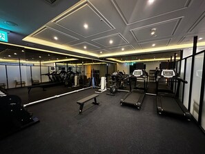 Een sportschool met loopbanden, gewichtapparaten en een bank.