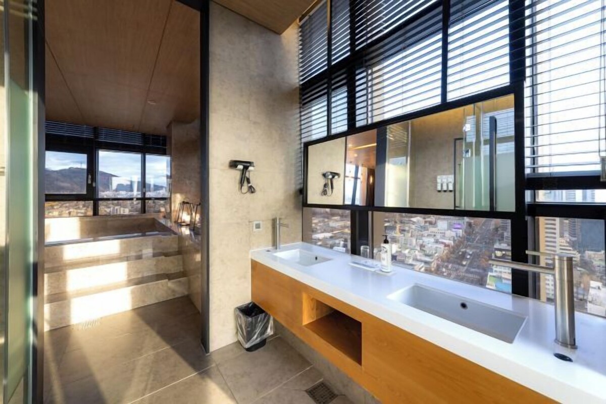 A modern bathroom with a large window, a white sink, and a wooden vanity.