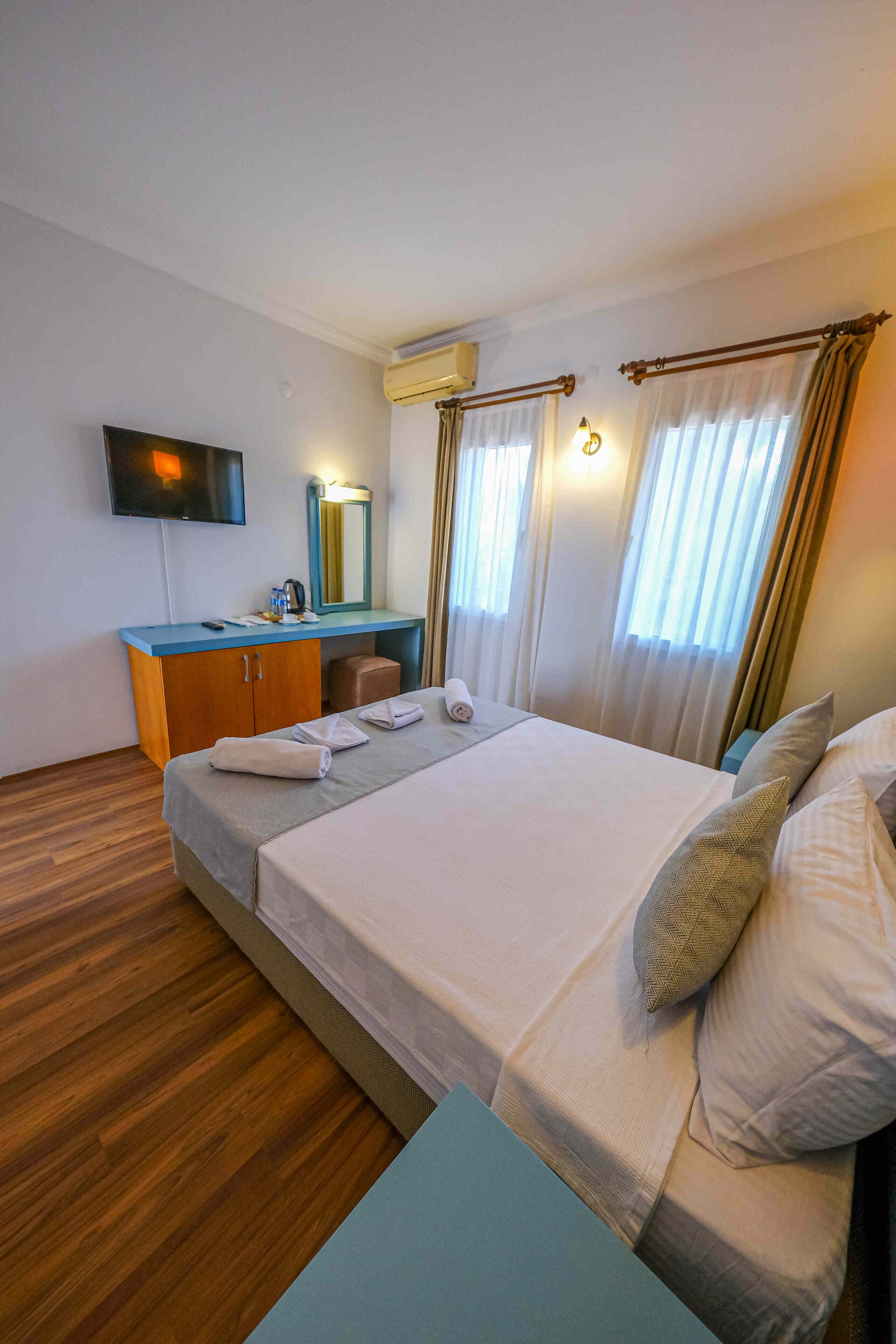 A hotel room with a bed, a desk with a mirror, a television, and curtains.